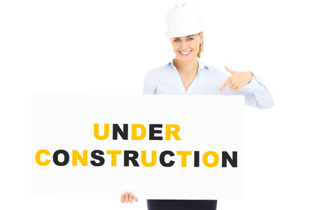 A picture of a pretty woman in a hard hat showing a banner with under construction inscriptionの写真素材