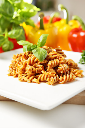 A picture of Italian pasta with red pepper pesto served on a white plate and decorated with basilの写真素材