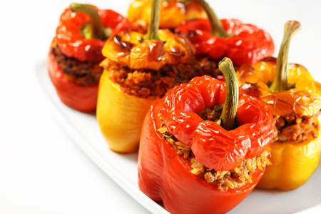 A picture of red and yellow stuffed peppers baked and served on a white plateの写真素材