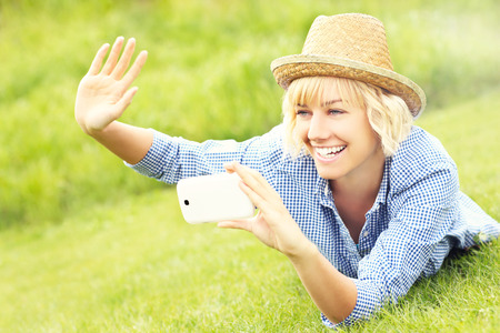 A picture of a woman lying on grass and taking pictures with cellphoneの写真素材