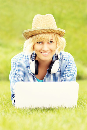 A picture of a happy woman with laptop lying on grassの写真素材