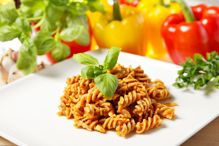A picture of Italian pasta with red pepper pesto served on a white plate and decorated with basilの写真素材