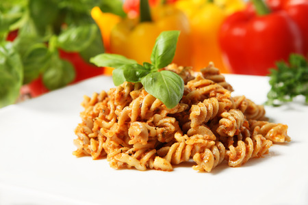 A picture of Italian pasta with red pepper pesto served on a white plate and decorated with basilの写真素材