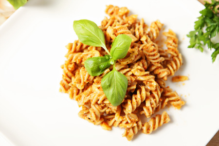A picture of Italian pasta with red pepper pesto served on a white plate and decorated with basilの写真素材