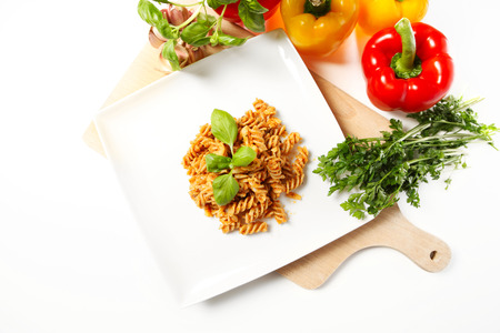 A picture of Italian pasta with red pepper pesto served on a white plate and decorated with basilの写真素材