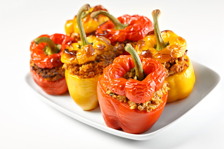 A picture of red and yellow stuffed peppers baked and served on a white plateの写真素材