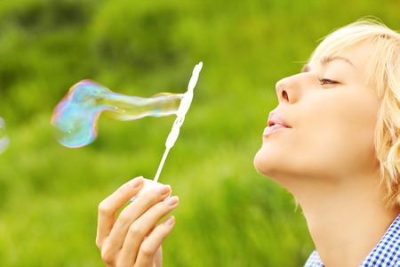 A picture of a beautiful woman blowing soap bubbles over green backgroundの写真素材