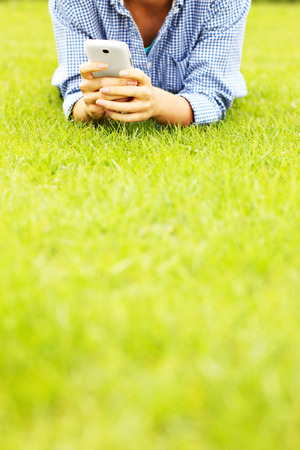 A picture of a woman with cellphone lying on grassの写真素材