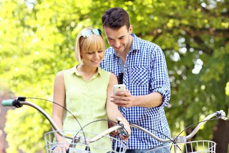 A picture of a young couple on bikes with a cellphoneの写真素材