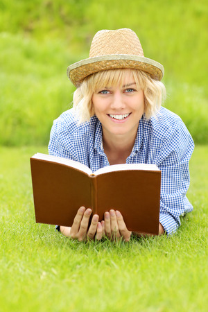 A picture of a young woman on a grass with a bookの写真素材