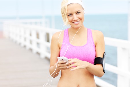 Young woman with phone listening music on pierの写真素材
