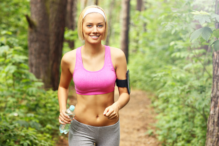 A picture of a woman jogging in the forest with a bottle of waterの写真素材