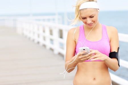 Young fit woman with phone on the pierの写真素材