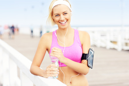 Young fit woman with water on the pier in pink sports bra and white bandの写真素材