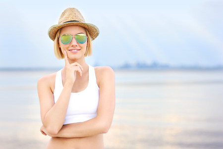 Young nice woman in hat and sun glasses standing over sea on the beachの写真素材