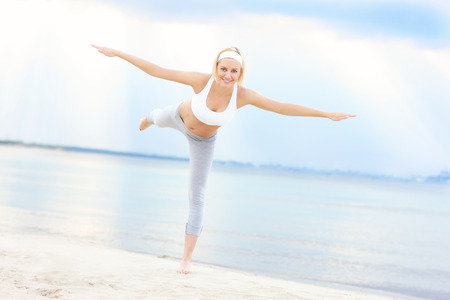 Young woman exercising on the beach over skyの写真素材