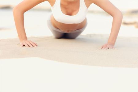 A midsection of a woman doing push-ups at the beachの写真素材