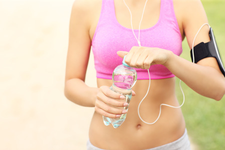 A midsection of a jogger opening bottle of water in the parkの写真素材
