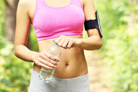 A midsection of a jogger opening bottle of water in the parkの写真素材