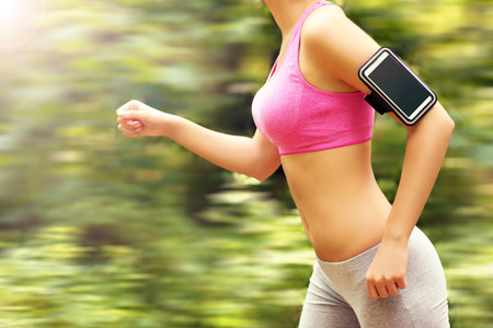 A midsection of woman jogging in the forest with smartphoneの写真素材