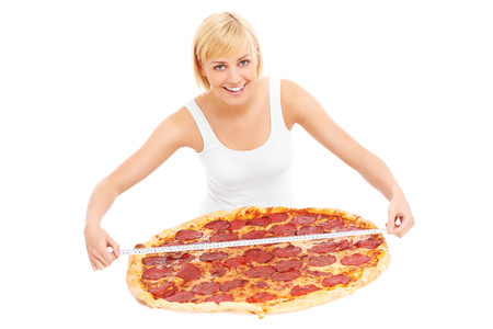 A picture of a happy woman measuring a huge pizza over white backgroundの写真素材