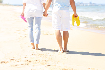 A picture of a couple walking at the beach and carrying flip flopsの写真素材