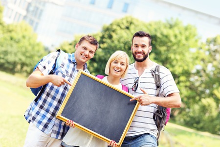 A picture of a group of students standing in the park and holding a blackboardの写真素材