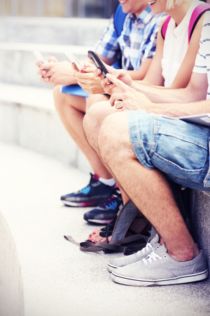 A picture of students sitting on stairs with their smartphonesの写真素材