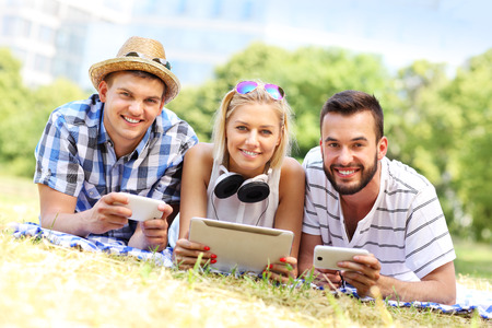 A picture of a group of friends using tablet and smartphones in the parkの写真素材