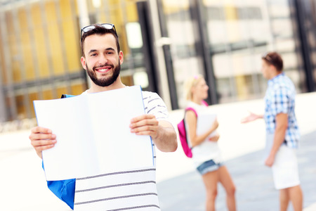 A picture of a young student standing in the campus with an open notebookの写真素材