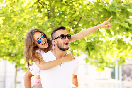 A picture of a happy couple doing piggyback and pointing at something in the parkの写真素材