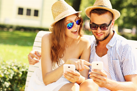 A picture of a young couple sitting on a bench with smartphonesの写真素材