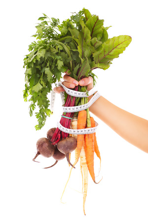 A picture of a hand holding raw carrots and beetroots tied with a tape measureの写真素材