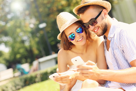 A picture of a happy couple with smartphones in the parkの写真素材