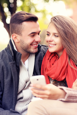 A picture of a young couple on a bench with smartphone in the parkの写真素材