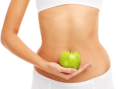 A midsection of a woman holding an apple over her bellyの写真素材