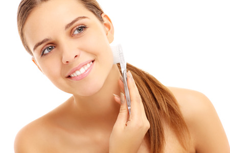 A picture of a young woman cleaning face with a brush over white backgroundの写真素材
