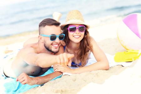 A picture of a happy couple pointing at something at the beachの写真素材