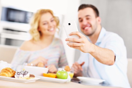 A picture of a young couple eating breakfast in the kitchen and taking selfieの写真素材