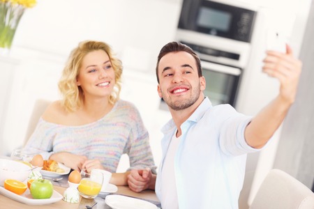 A picture of a young couple eating breakfast in the kitchen and taking selfieの写真素材
