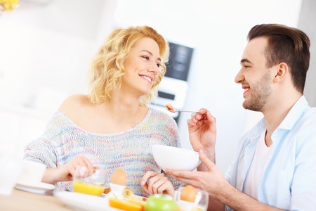 A picture of a young couple eating breakfast in the kitchenの写真素材