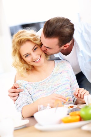 A picture of a young man giving a good morning kiss to his wife in the kitchenの写真素材