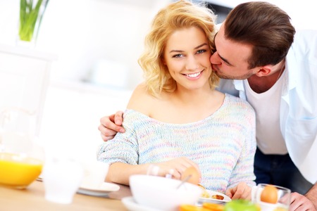 A picture of a young man giving a good morning kiss to his wife in the kitchenの写真素材