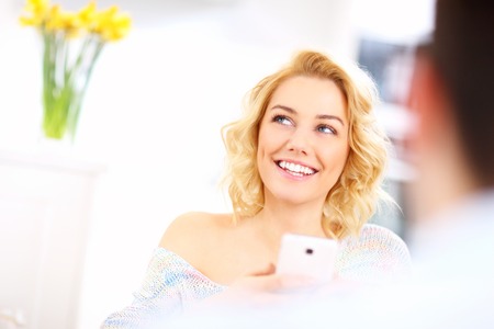 A picture of a young happy woman texting in the kitchenの写真素材