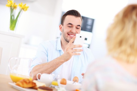 A picture of a young couple eating breakfast and taking pictures in the kitchenの写真素材