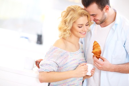 A picture of a young couple eating breakfast and hugginh in the kitchenの写真素材
