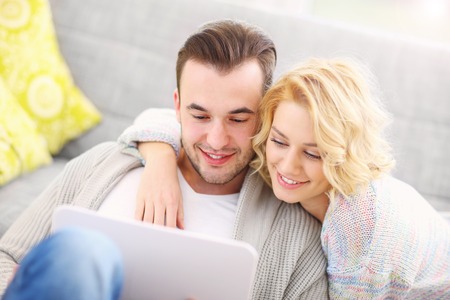 A picture of a romantic couple with laptop in living roomの写真素材