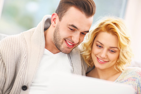 A picture of a romantic couple with laptop in living roomの写真素材