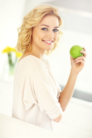 A picture of a young woman eating apple in the kitchenの写真素材