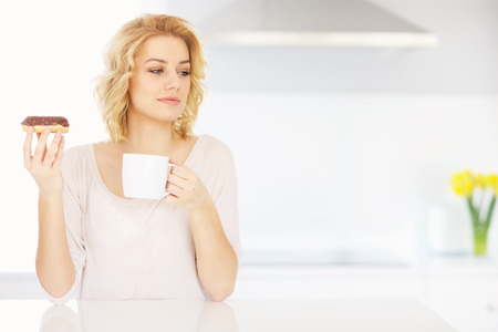 A picture of a young woman eating donut with morning coffeeの写真素材